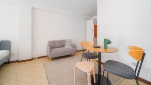 En lille, moderne stue med en grå sofa, et rundt bord med to stole og en mindre måtte på gulvet.