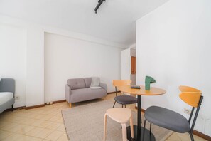 Un petit salon moderne avec un canapé gris, une table ronde accompagnée de deux chaises et un petit tapis sur le sol.