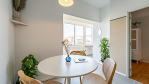 A modern dining area with a round table, four chairs, a vase with dried plants, and a pendant light.