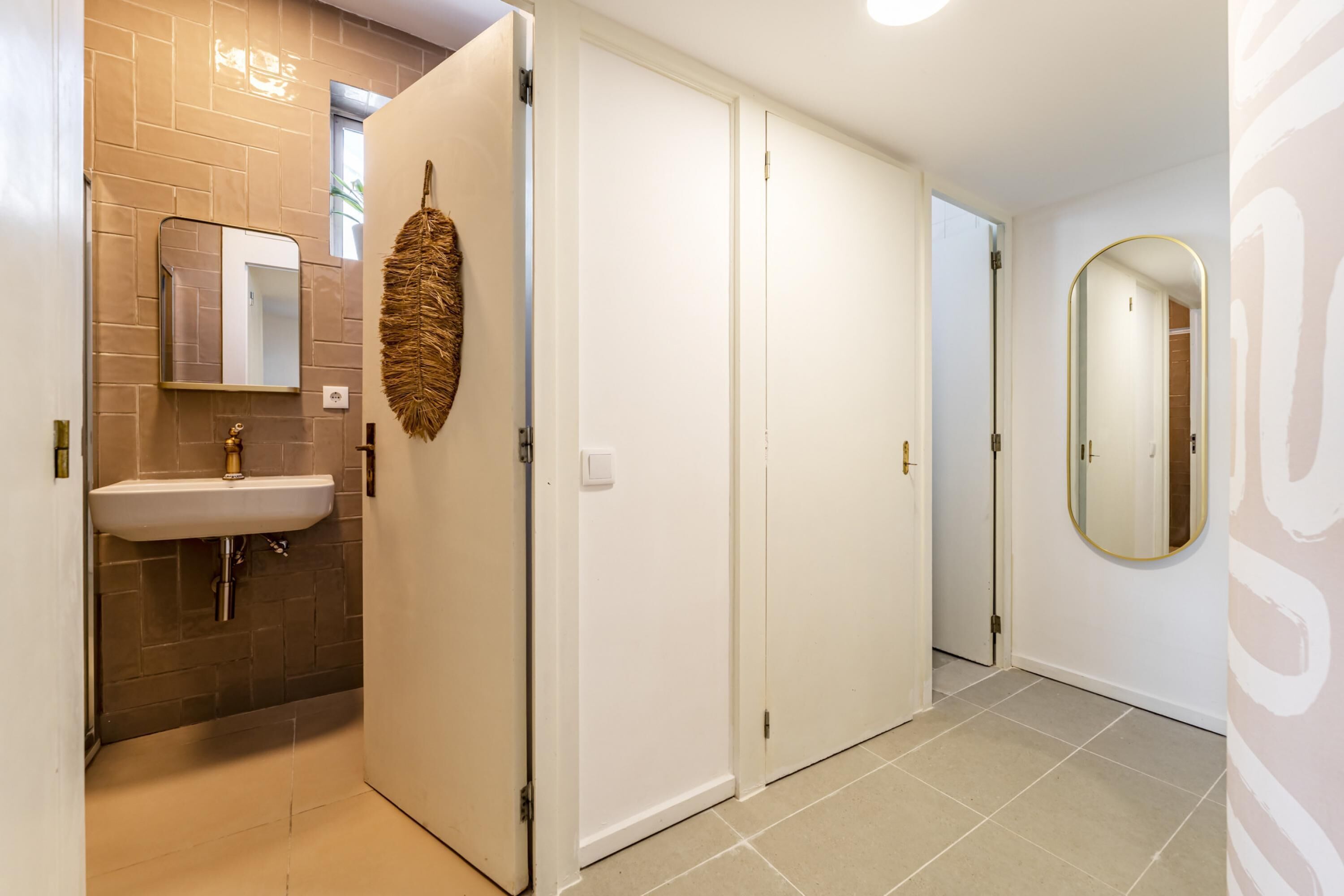 Een badkamer met een wastafel, spiegel en een deur naar een andere ruimte.