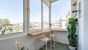 A corner room with a view of a cityscape, two chairs, a potted plant, and a window sill.