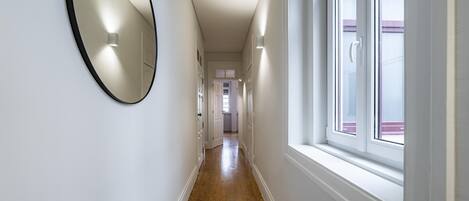 A hallway with a wooden floor, white walls, a large mirror, and a window.