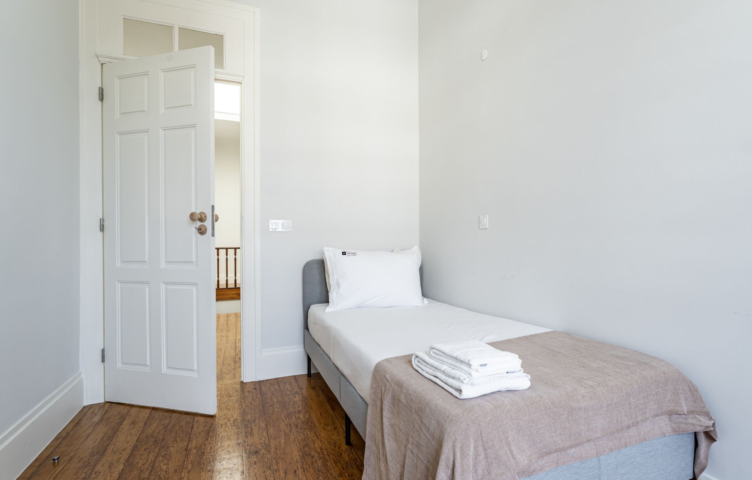 Ein Schlafzimmer mit einem Einzelbett, einer Tür zu einem anderen Raum und Holzboden.