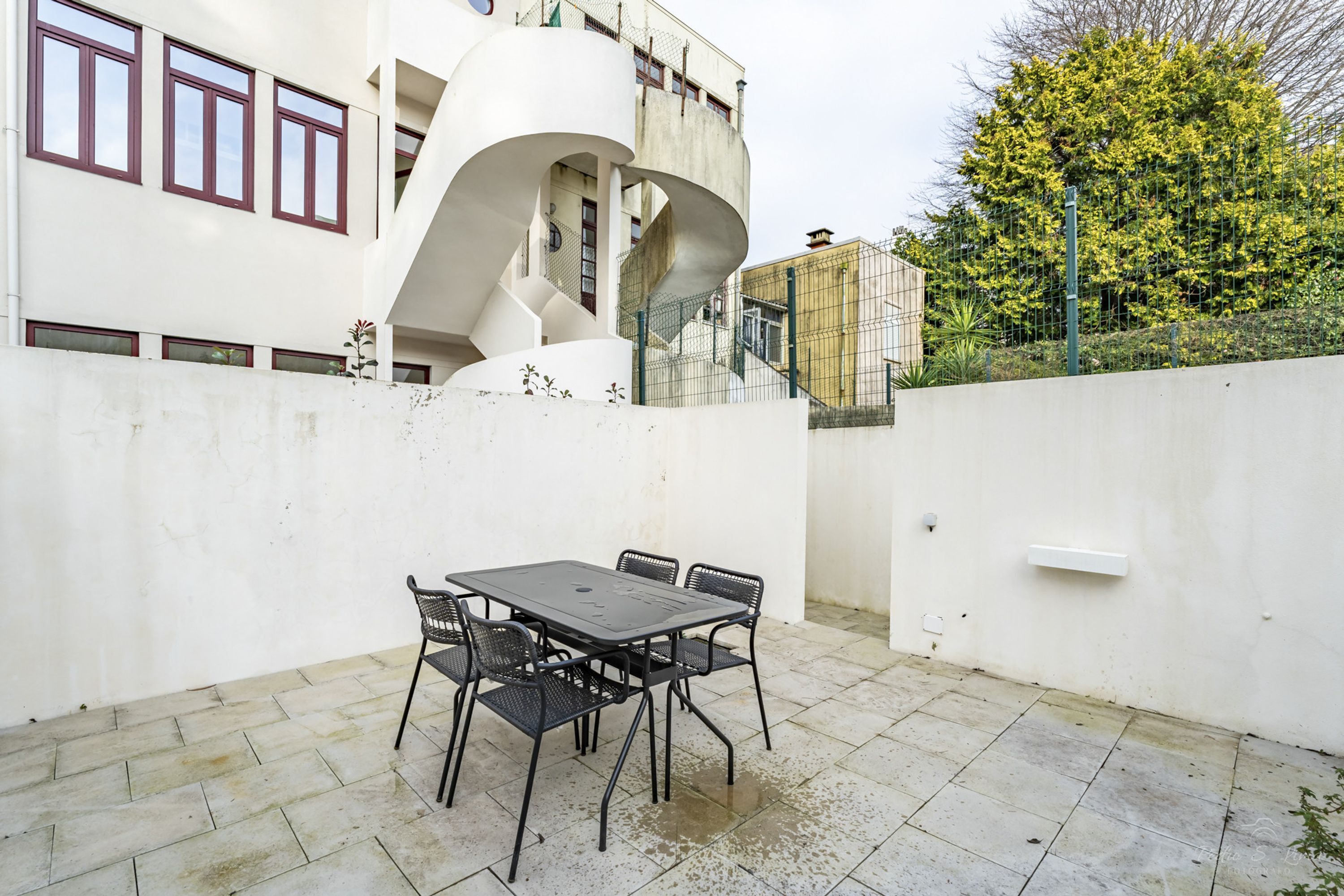 A patio with a table and chairs, a white wall, and a staircase leading to a building.
