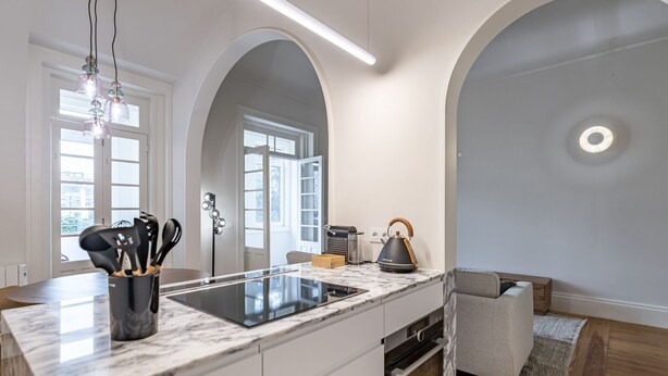 A modern kitchen with a marble countertop, a built-in oven, and a coffee machine. There are two pendant lights and a large window with a view of the city. - Nomad s Family - 3bdr City Vibe Porto (Porto)