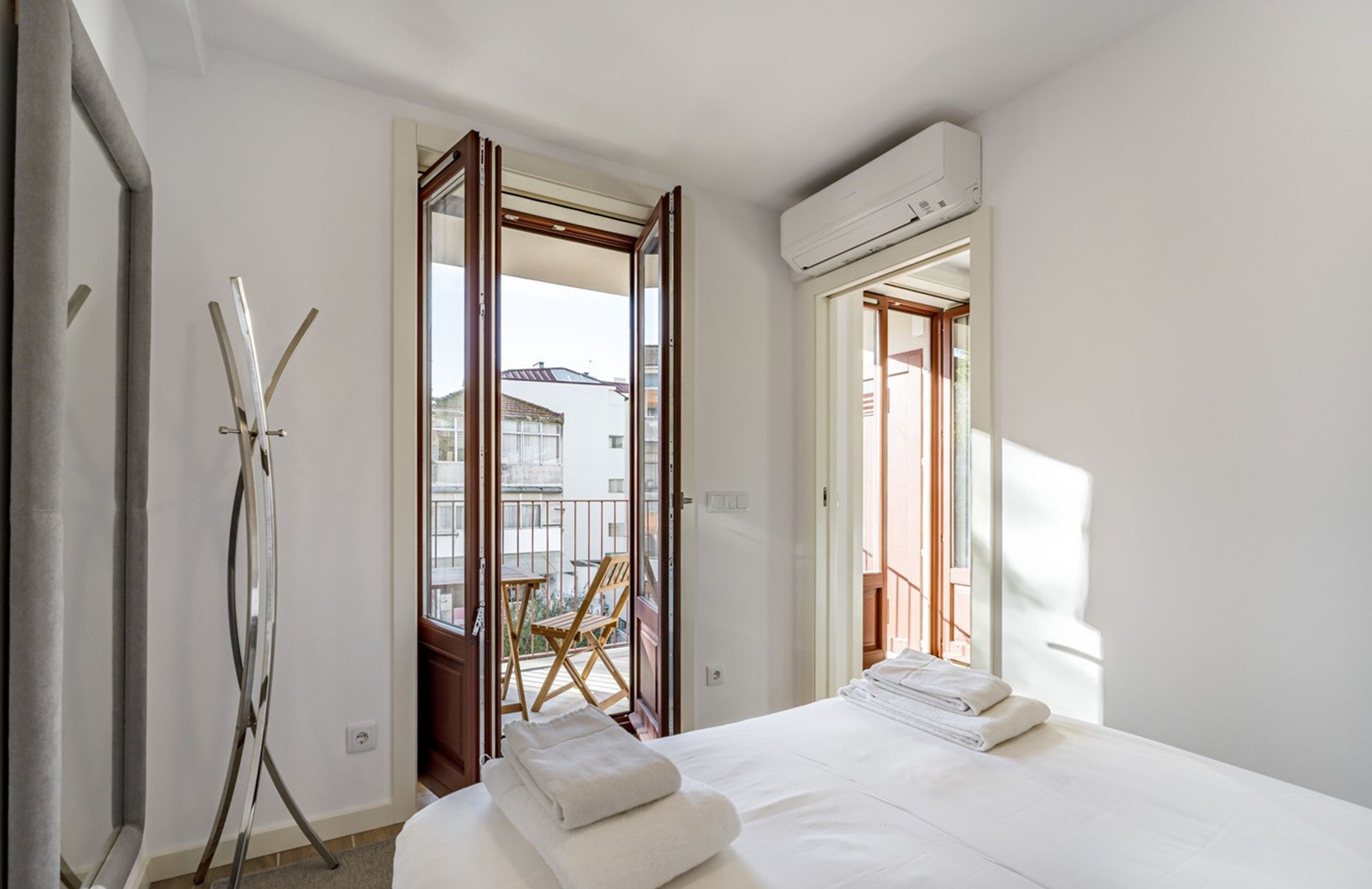 A hotel room with a bed, a chair, and an open door leading to a balcony.