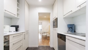Una cocina estrecha con gabinetes blancos, microondas, cafetera y lavavajillas.