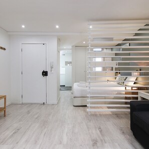 Una habitación moderna y minimalista con una puerta blanca, una cama con cabecera blanca, un sofá negro y una escalera con barandilla blanca.