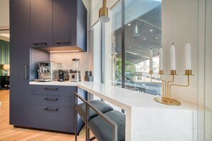 Une cuisine moderne avec des meubles de couleur sombre, un plan de travail blanc et une machine à café.