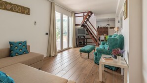A spacious living room with a wooden staircase, a sofa, a green armchair, and a small table with a book and flowers. - Villa Giovanna con Piscina by Wonderful Italy (Castellammare del Golfo)