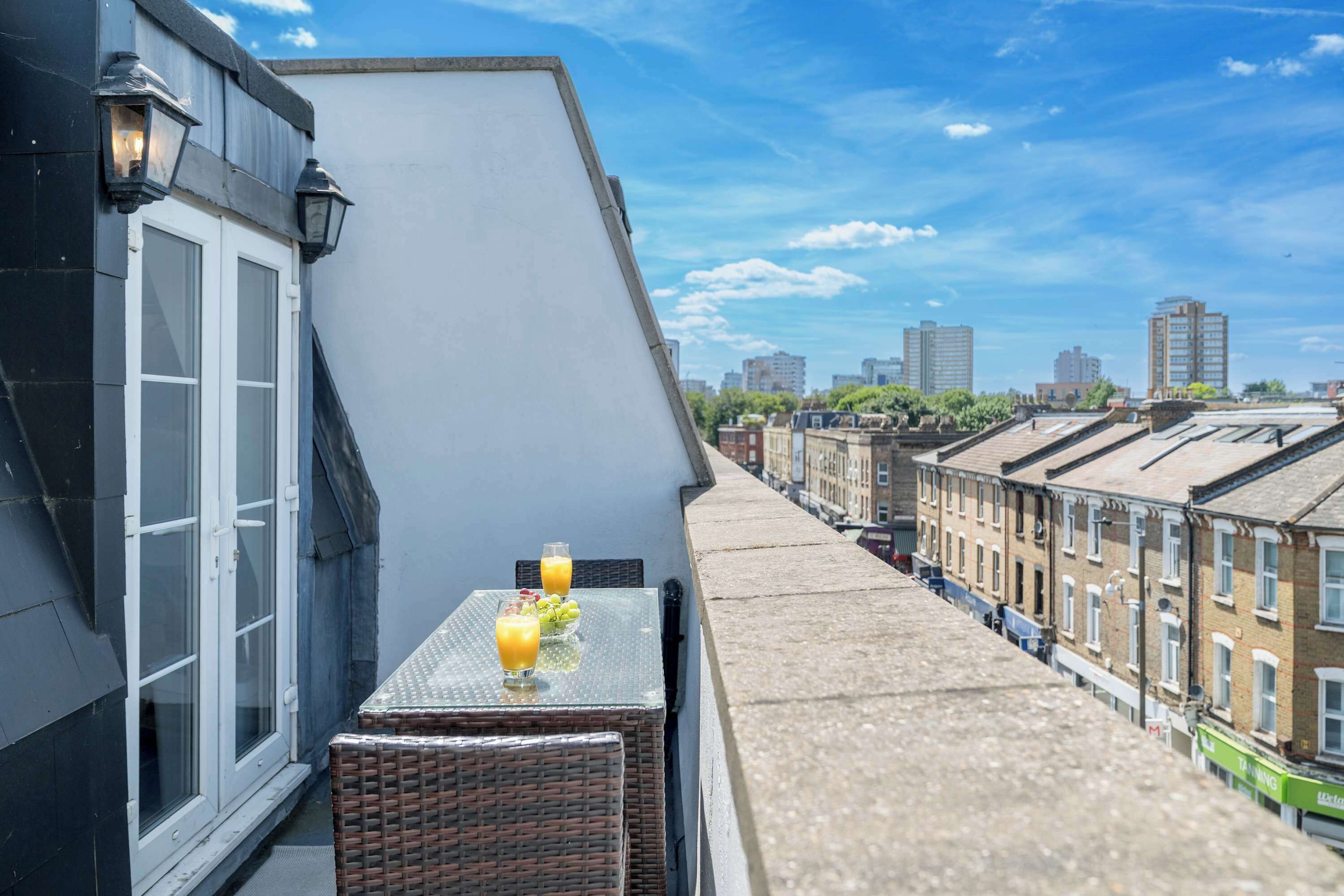 A balcony with a table, two glasses of orange juice, and a wicker chair.