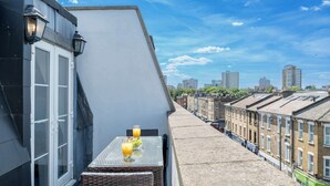 A balcony with a table, two glasses of orange juice, and a wicker chair. - Battersea Park 7 Min walk • Balcony • Cafés Below (London)