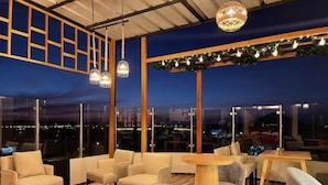 A rooftop lounge with seating and tables, large windows, and decorative lighting. - Hostal Macacona  (Subtanjalla)