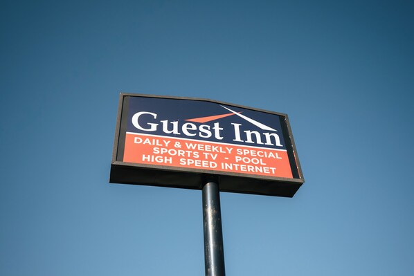 Señal de un hotel llamado "Guest Inn" con servicios que incluyen ofertas diarias y semanales, televisión para deportes, piscina e internet de alta velocidad.