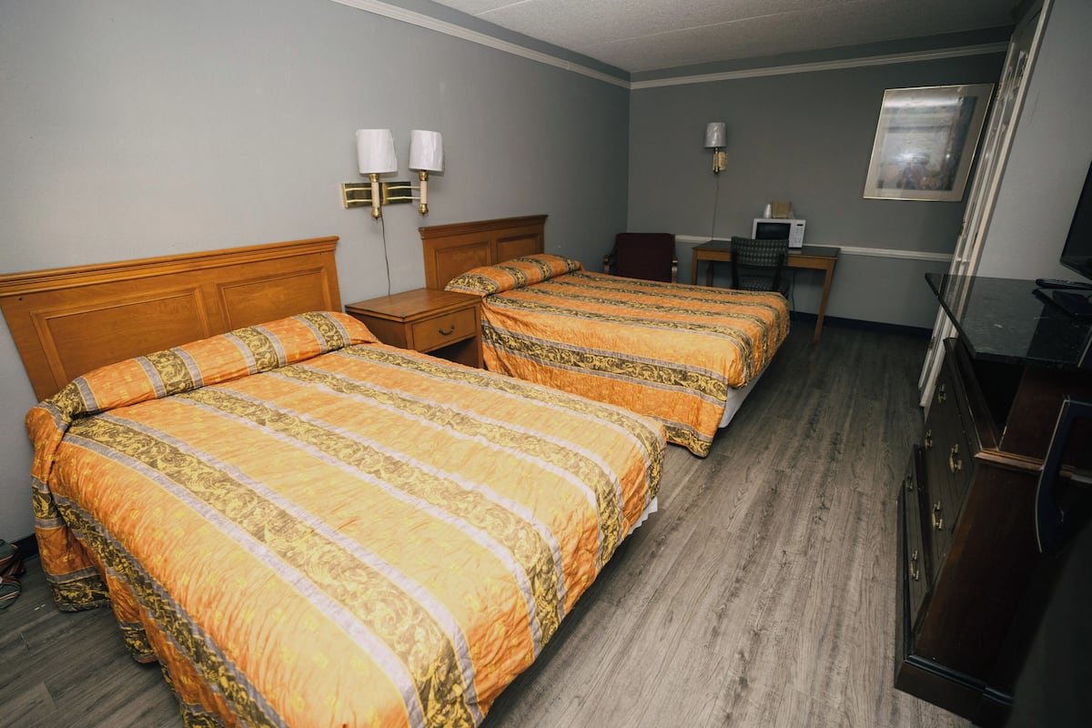 A hotel room with two beds, a desk, a television, and a microwave.