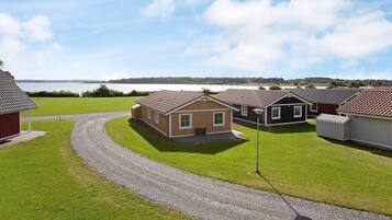 A row of single-story houses with a gravel driveway leading to a grassy area, a body of water in the background, and a clear sky.