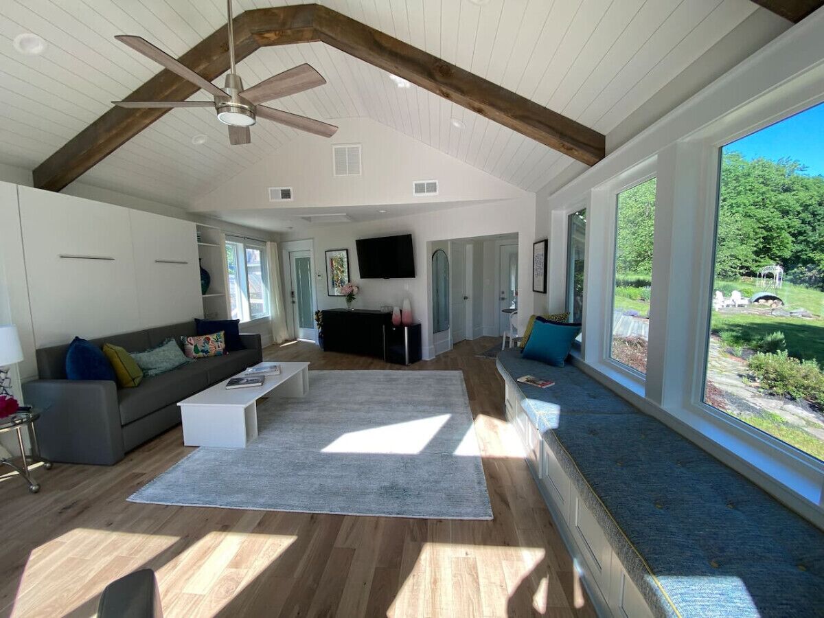 Un salon spacieux doté d’un plancher en bois, d’un ventilateur de plafond, d’une grande fenêtre et offrant une vue sur l’extérieur.