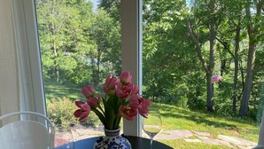 Taula amb un ram de flors roses i dues copes de vi, davant d'una finestra amb vista a un jardí.