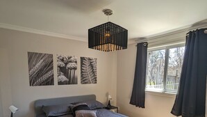 A bedroom with a bed, a nightstand, a lamp, and a window with curtains. - Appartement Style Urbain Très Tranquille Situés a 5 min du Vieux Terrebonne (Laval)