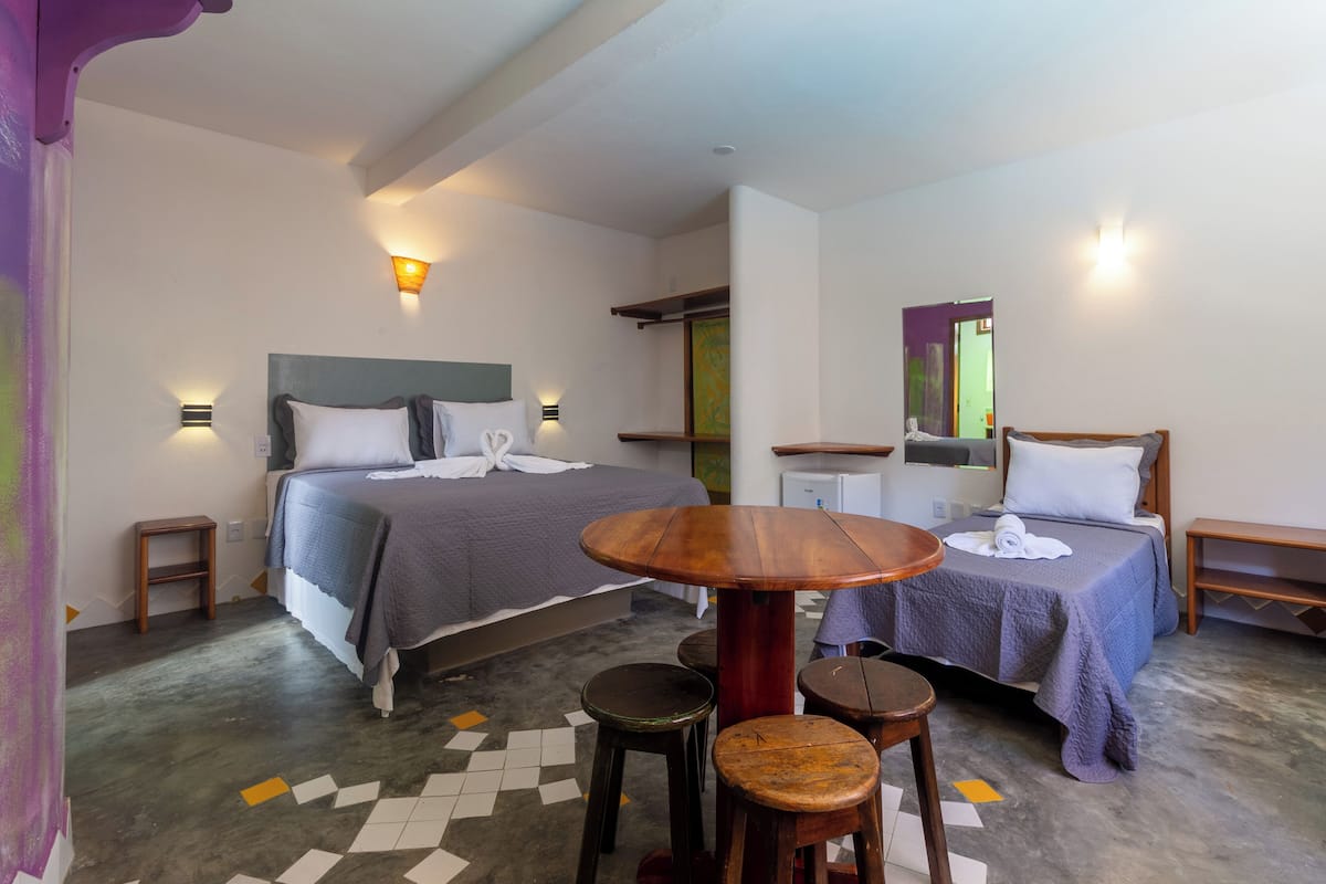 A hotel room with two beds, a small round wooden table, two stools, and a mirror.