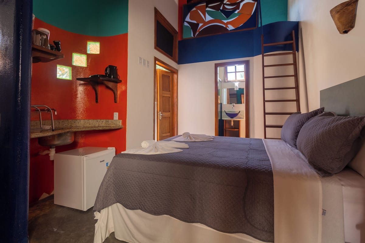 A hotel room with a bed, a small white refrigerator, a sink, and a window.