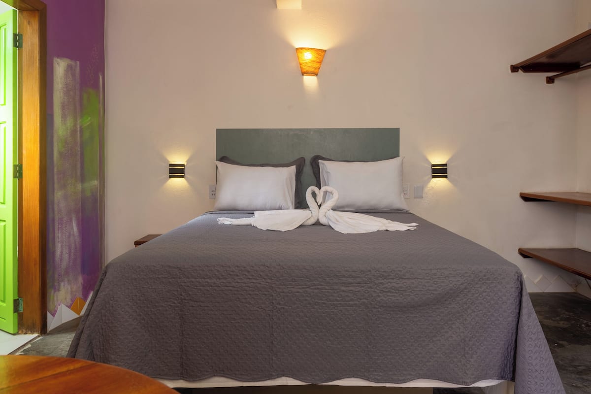 A neatly made bed with a grey quilt, two bedside lamps, and a wall-mounted light fixture.
