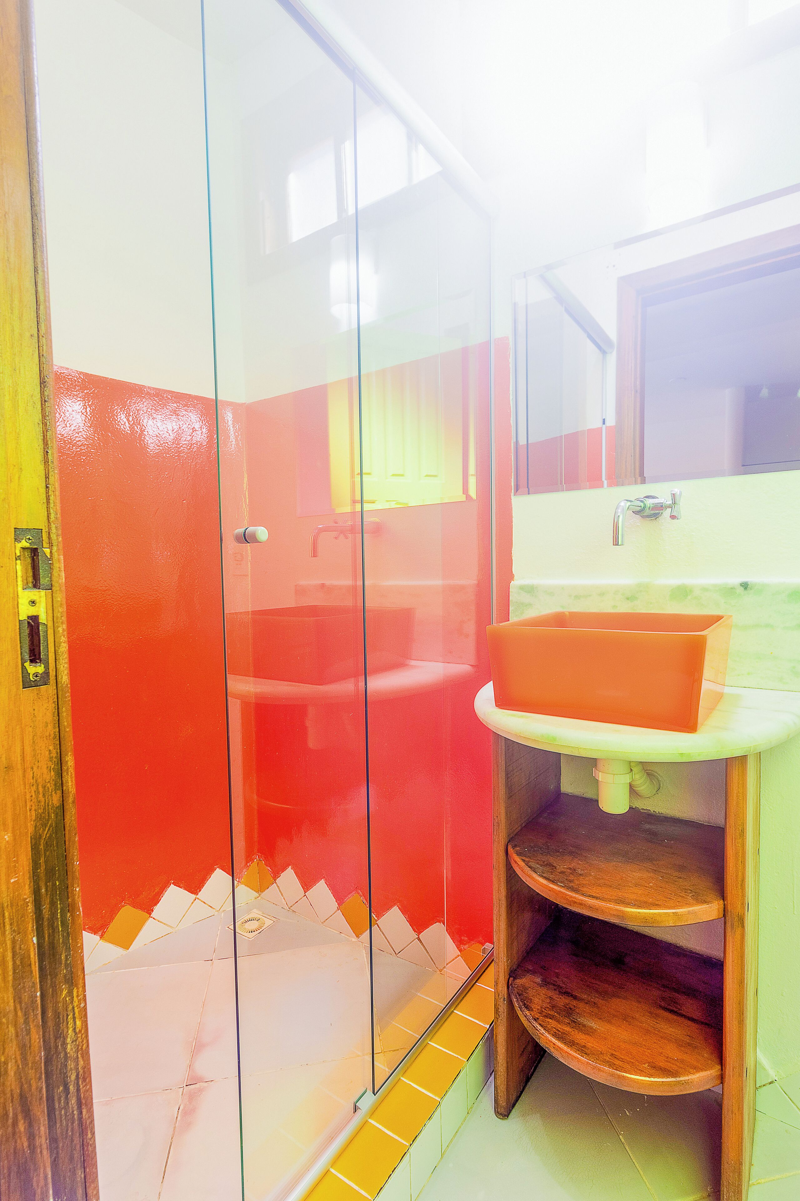 Ein Badezimmer mit Duschkabine aus Glas, einem Waschbecken mit roter Schüssel und einem hölzernen Regal.