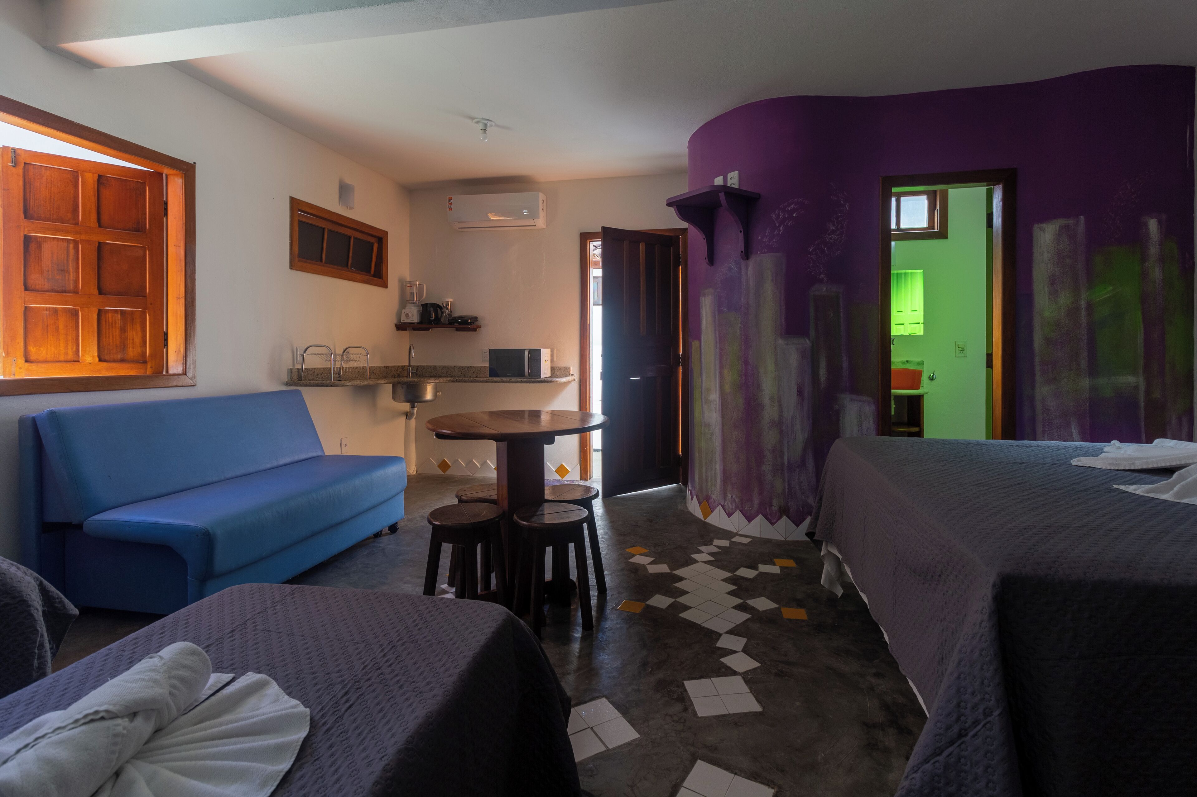 Camera d'albergo con divano blu, un letto, un piccolo tavolo con sgabelli e un angolo cottura con microonde.