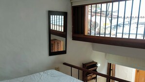 Ein Schlafzimmer mit einem Bett, einem Holztisch, einem Spiegel und einem Fenster mit Blick ins Freie.