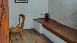 Ein kleiner Raum mit einem Holzbstuhl, einer Bank, einem gerahmten Bild an der Wand und einem Deckenventilator.