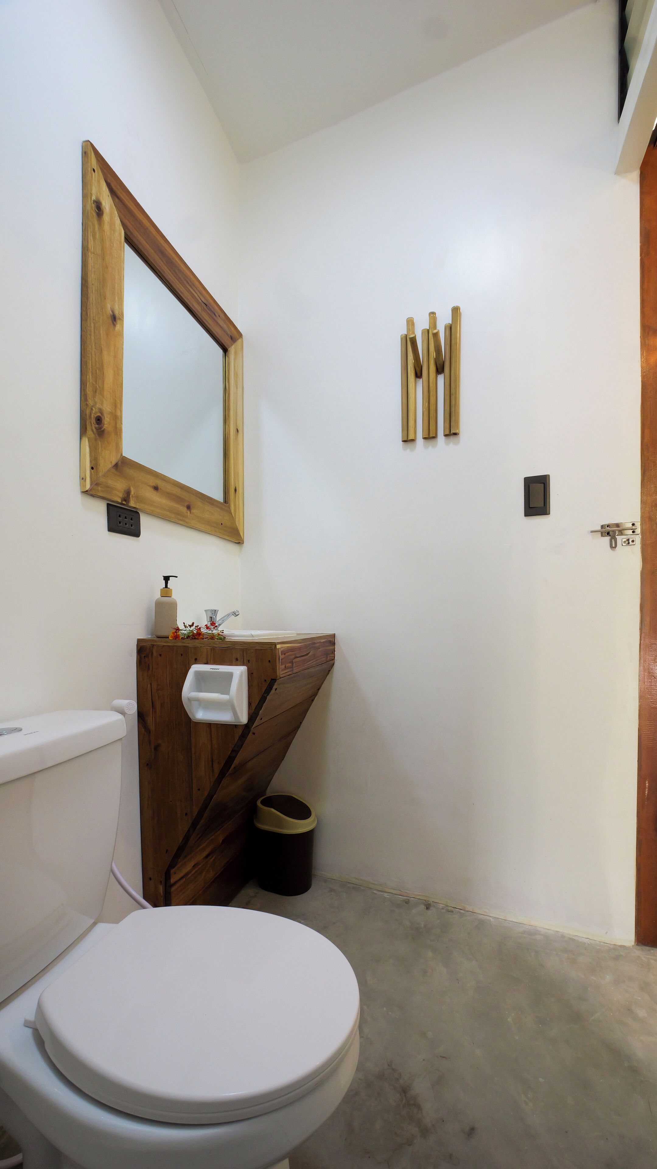 A bathroom with a wooden vanity, a toilet, a mirror, and a trash bin.