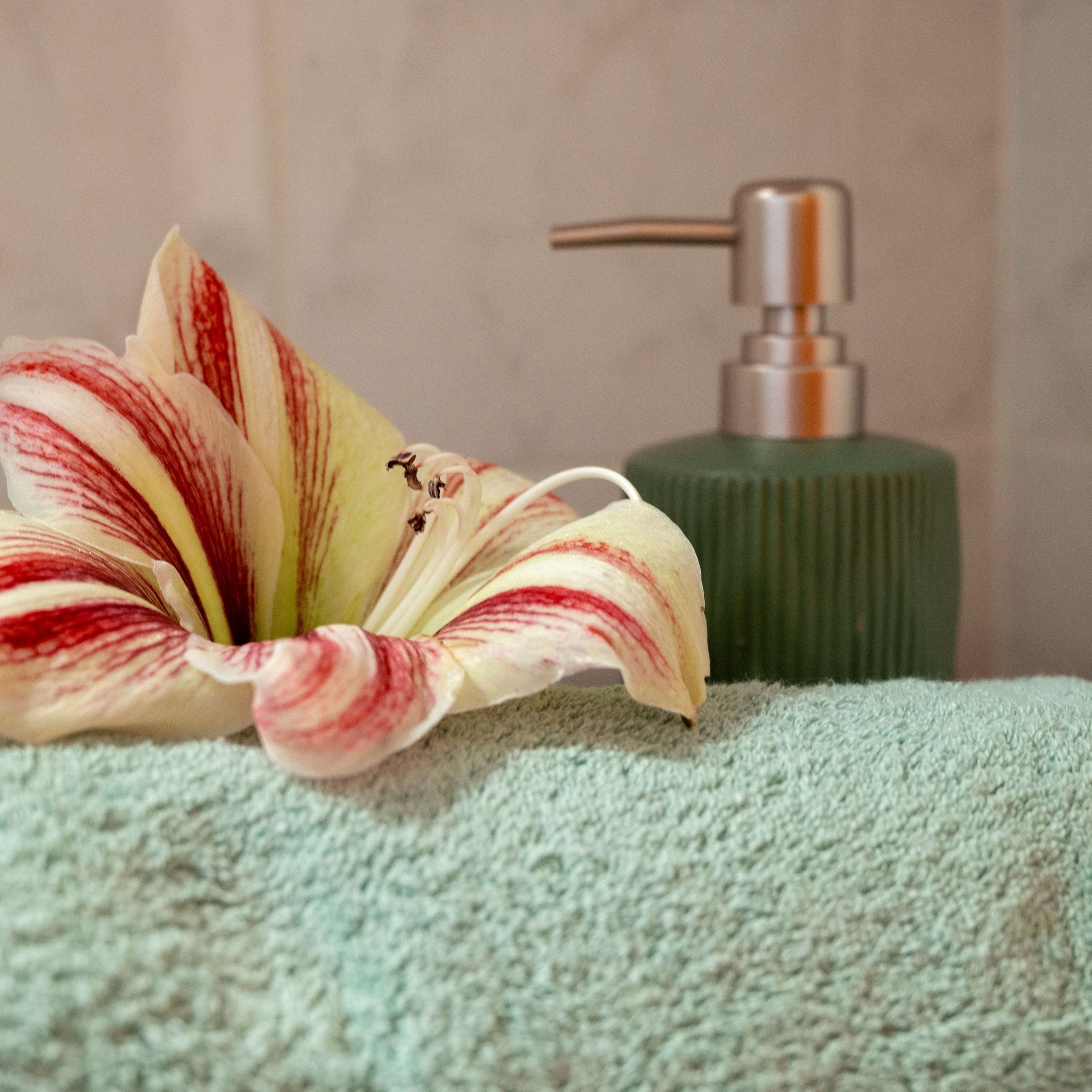 A bathroom with a green soap dispenser and a towel.