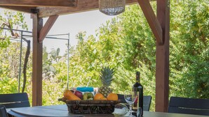 Un patio al aire libre con una mesa y sillas de madera, una cesta de mimbre con frutas, una botella y un vaso.
