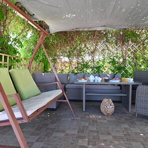 An outdoor seating area with a swing chair, cushioned seating, and a table set for breakfast.