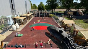 Een speelruimte met dinosaurus thema, met een grote krokodillensculptuur, een zwembad en een muurschildering van een waterval.