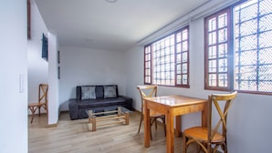 Ein Zimmer mit Esstisch und Stühlen, einer Couch und großen, fensterartigen Rasterelementen.