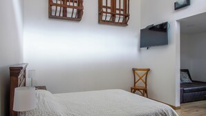 Ein Schlafzimmer mit Bett, Sessel, Fernseher und einem kleinen Tisch mit Lampe.