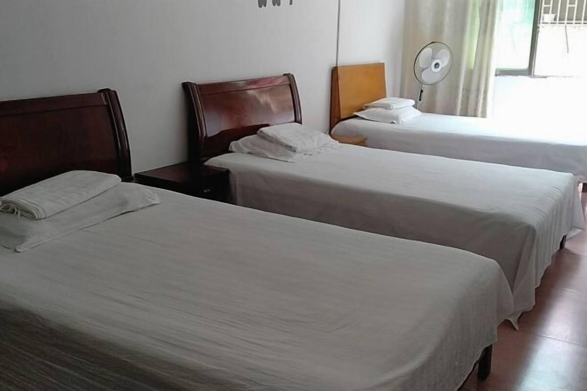 A hotel room with two single beds, a bedside table with a lamp, and a window with a curtain.