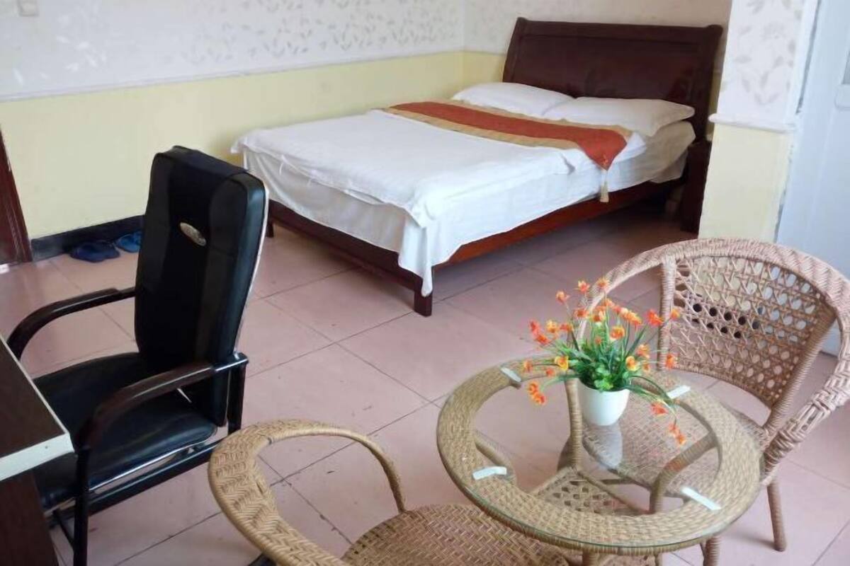 A bedroom with a bed, a chair, a table with flowers, and a desk.