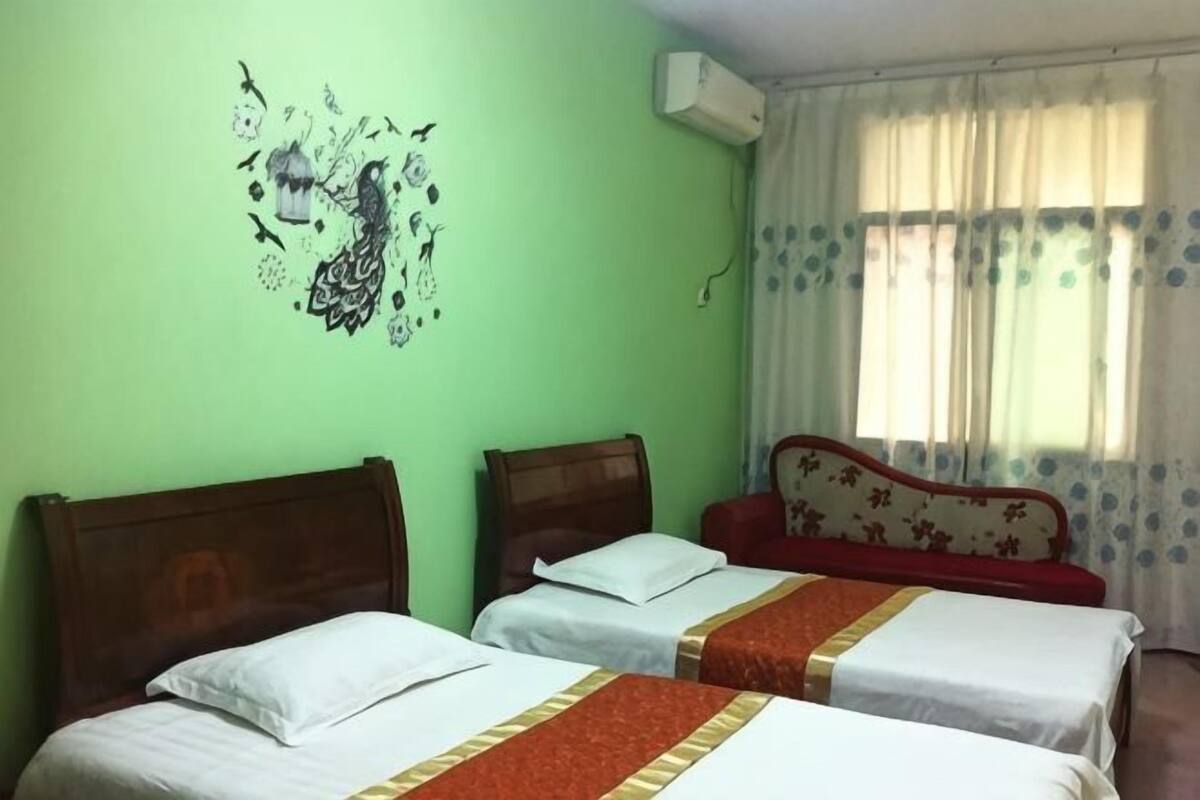 A room with two beds, a decorative wall art, a window with curtains, and an air conditioning unit.