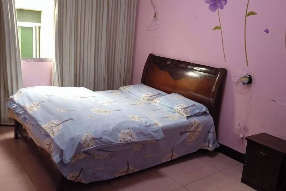 A bedroom with a bed, curtains, a wooden headboard, and a wall with a flower decal.