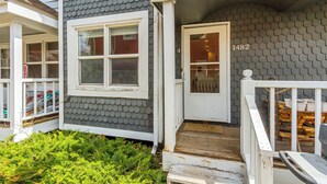 Una casa con revestimiento de tejas grises, una puerta principal blanca y un pequeño porche con barandilla de madera.