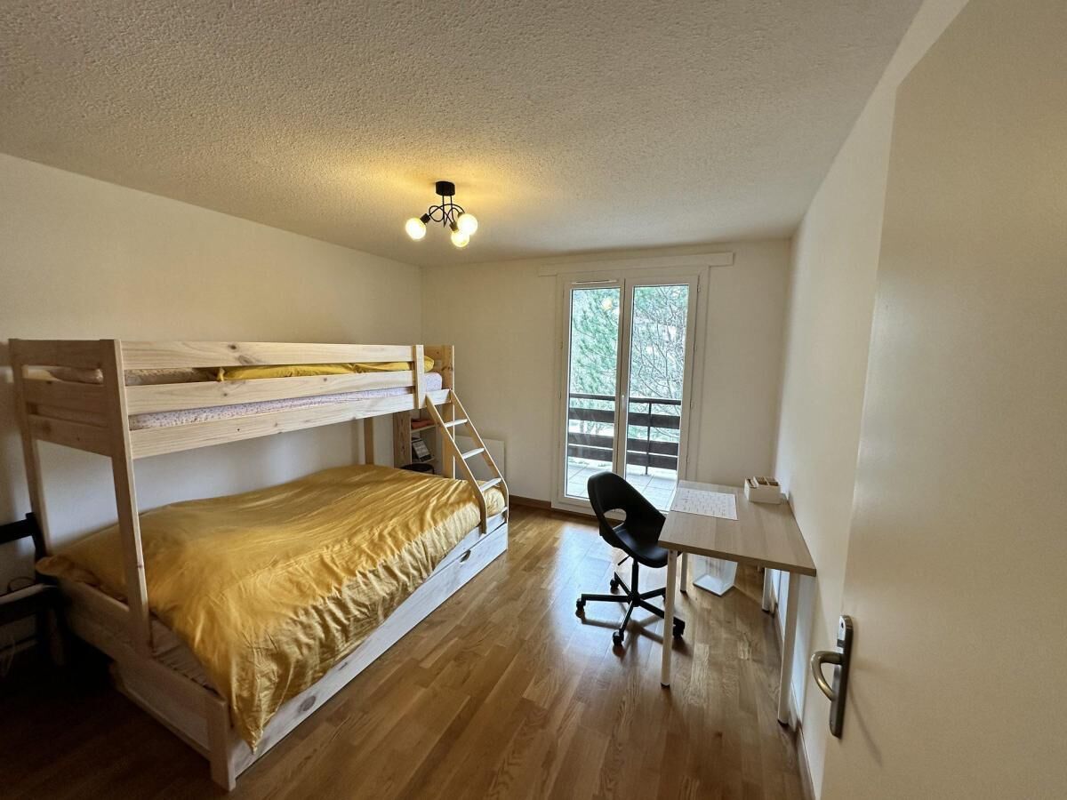 A bunk bed with a desk and chair, a window with a view of trees, and a ceiling light fixture.