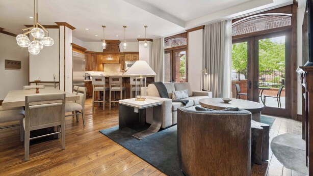 A spacious living area with a dining table, sofa, and coffee table, connected to a kitchen with wooden cabinets and a large window. - The Aspen 08ABC - 3 Bedroom Residence (Aspen)