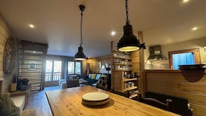 A wooden dining table with plates, hanging pendant lights, and a kitchen area with shelves and a stove. - Chalet, terrace, fireplace or stove, tv, 150m², Vars (Vars)