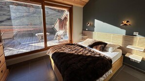 A bedroom with a large window, a bed with a dark blanket, wooden headboard, and a small bedside table with a lamp. - 5th floor, balcony, tv, ski locker, 65m², Vars (Vars)