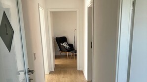 A narrow hallway with wooden flooring, white walls, and a black chair with a patterned cushion. - Borsch Holiday Apartment 2 (Geisa)