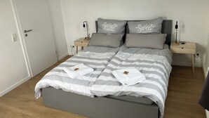 A neatly made bed with striped bedding and pillows, two bedside tables with lamps, and a door to the left. - Borsch Holiday Apartment 2 (Geisa)