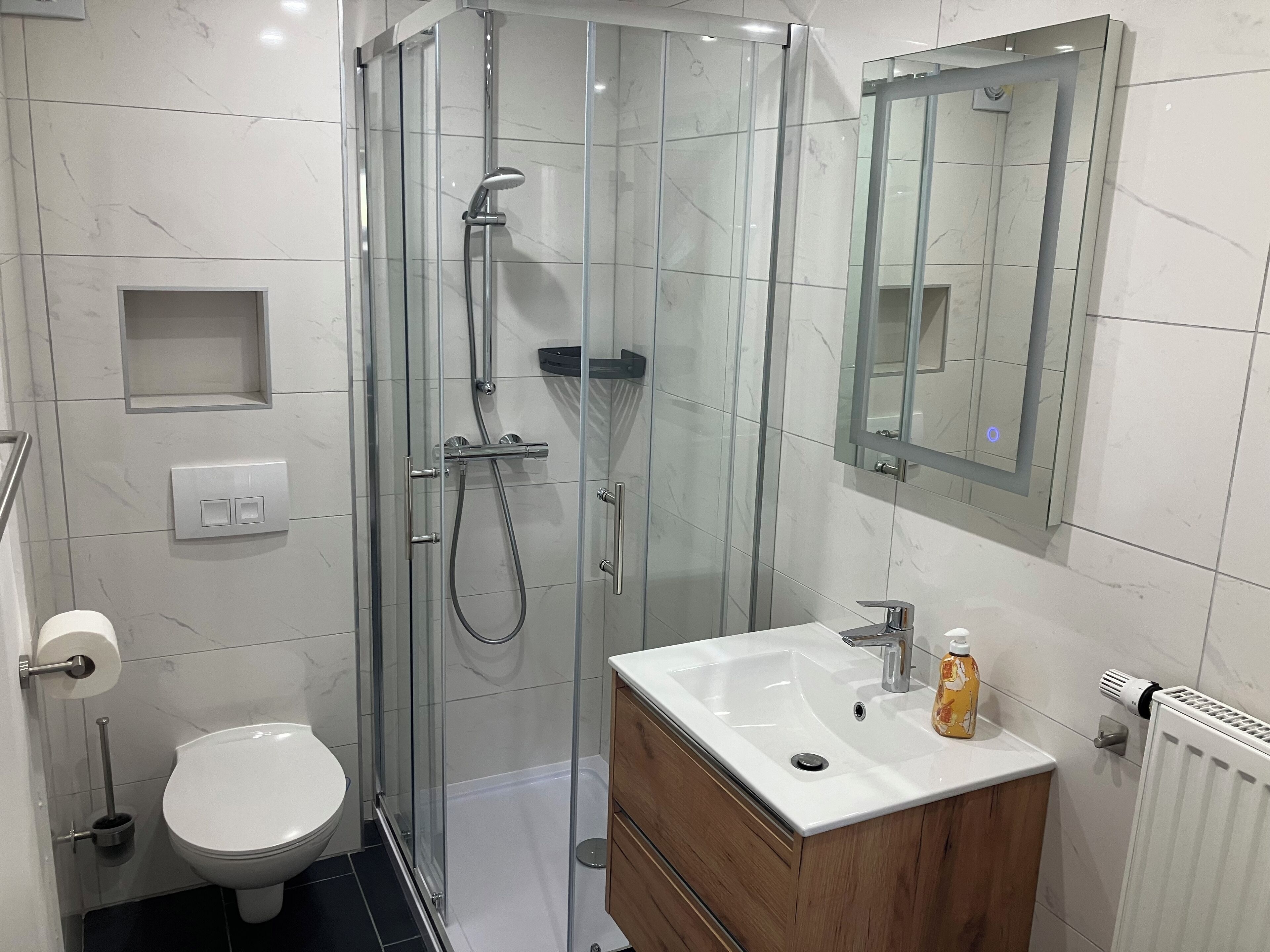 A modern bathroom with a glass-enclosed shower, a white sink with a wooden vanity, and a mirror above the sink.