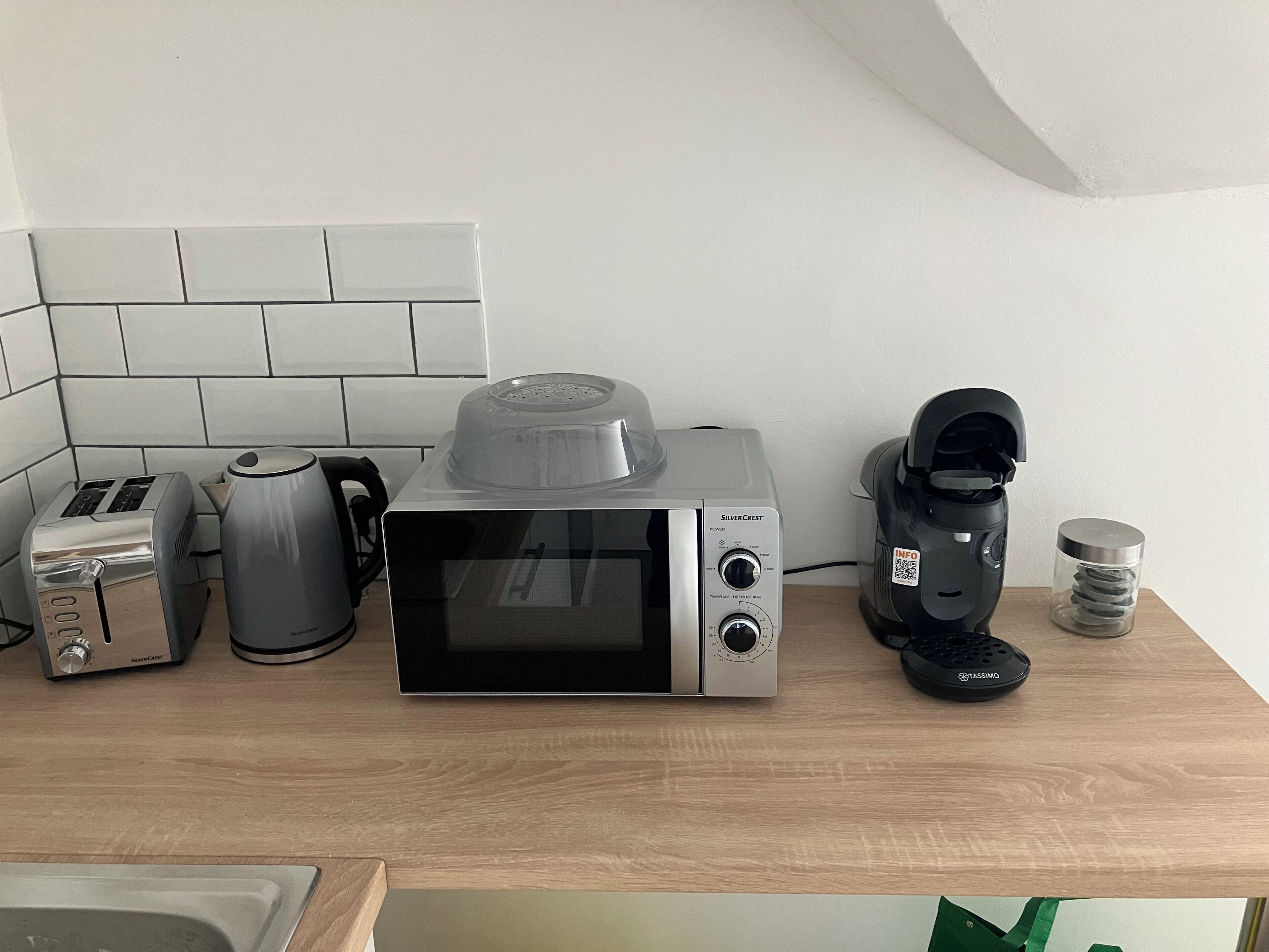 Une cuisine équipée d’un four à micro-ondes, d’un grille-pain, d’une machine à café et d’une bouilloire, le tout posé sur un plan de travail en bois.